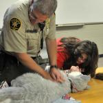 Sheriff Officer assists Genete in CPR demo. Sheriff's & Search & Rescue Units need this life-saving training for the K9s under their care. 